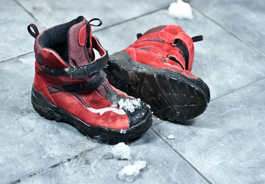 Dirty, snowy red boots on a tile floor.