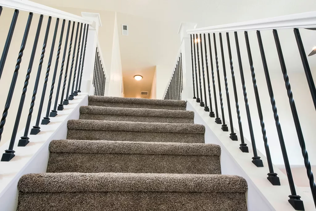 Carpeted stairs and banister with iron railing
